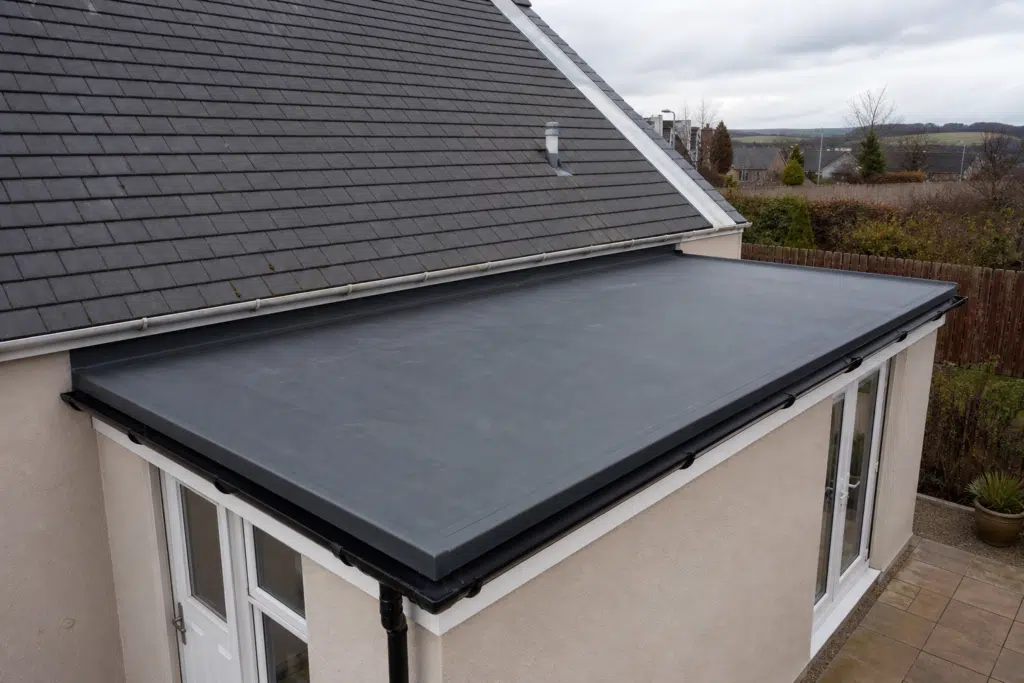 Residential flat-roof extension with a dark EPDM-style roofing membrane in a Scottish setting