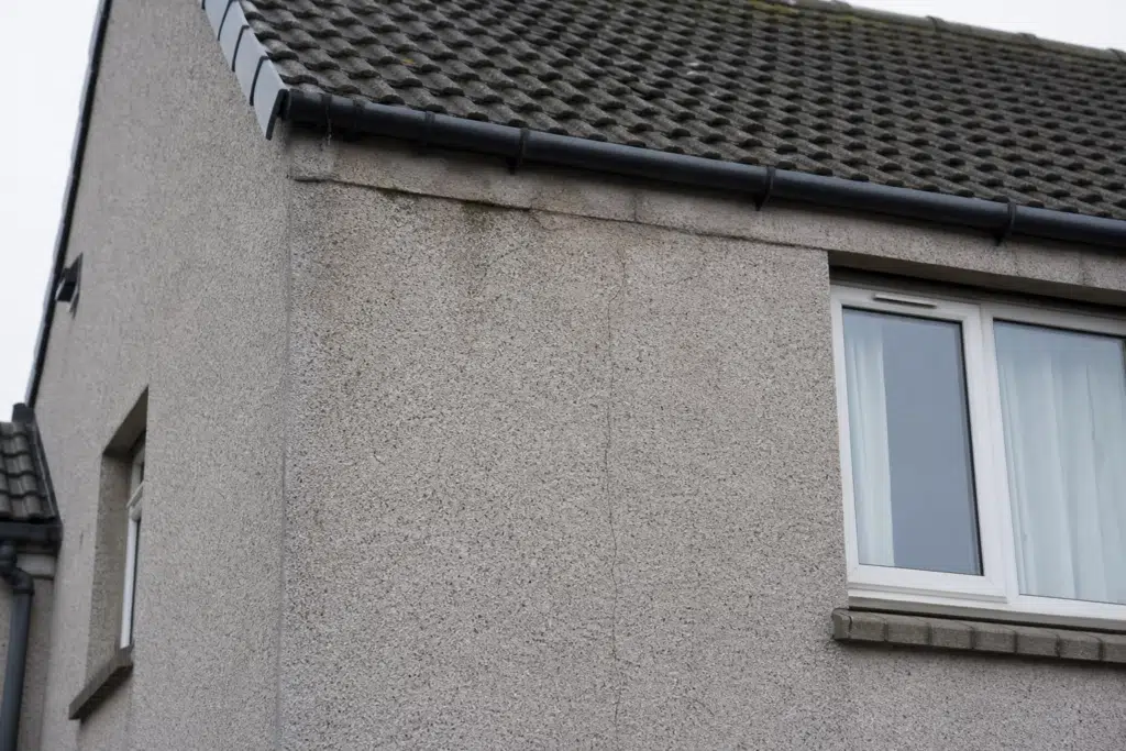 Textured roughcast exterior wall with a small visible crack beneath the roofline of a Scottish home